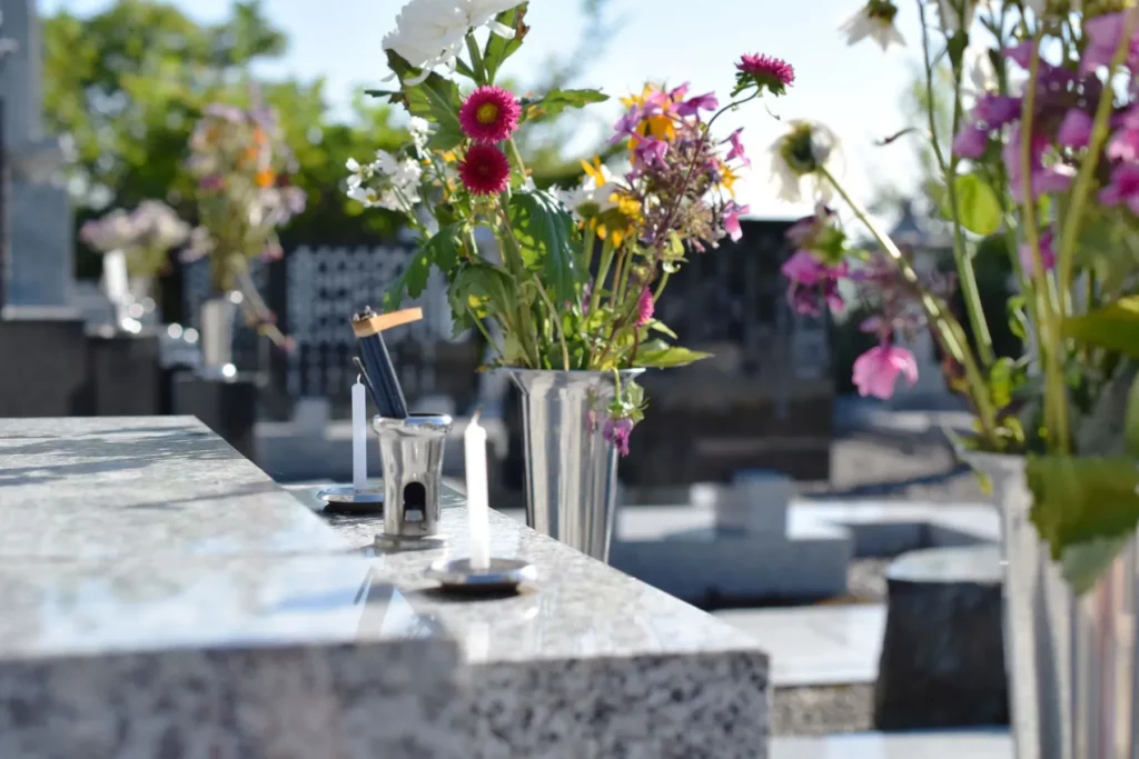 Gros plan sur une pierre tombale ornée de bougies et d'un vase de fleurs colorées.